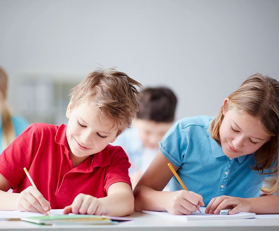 Two children are writing on paper at a table.