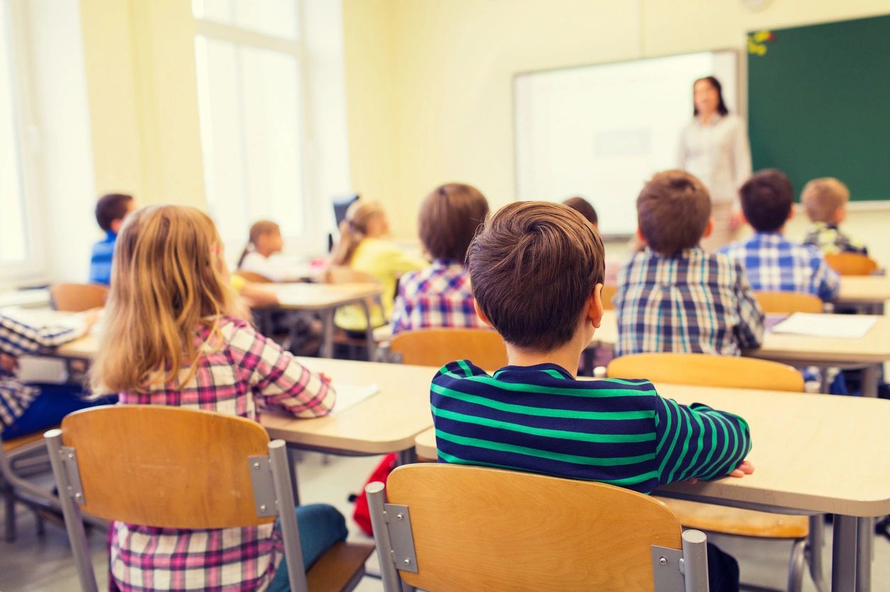 A group of children sitting at desks in front of a teacher.